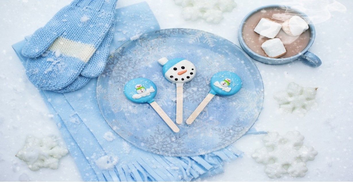 Blue plate with snowman and stocking cap Popsicles, atop a blue scarf and blue mittens