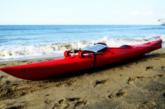 red kayak on the sandy beach, white waves and blue water behind kayak