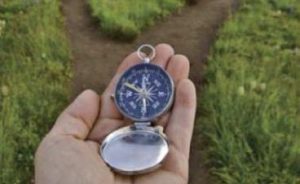 hand holding a compass in front of a fork in a road