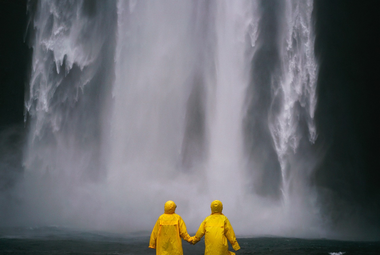couple in yellow rain coats holding hands in front of waterfall